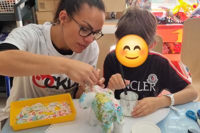 Un bénévole de l'Association Cékedubonheur aide un enfant hospitalisé à créer un éléphant avec la méthode déco patch lors d'un atelier créatif - Agrandir l'image 1 sur 3, fenêtre modale